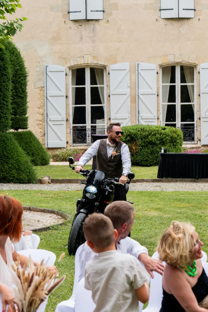 Photo du marié arrivant en moto à la cérémonie laïque au château du Croisillat à Caraman (31) - Mariage d’Élodie et Julien - 2025 - Photographe à Saint-Gaudens (31) Marc Villard / VILMAGE