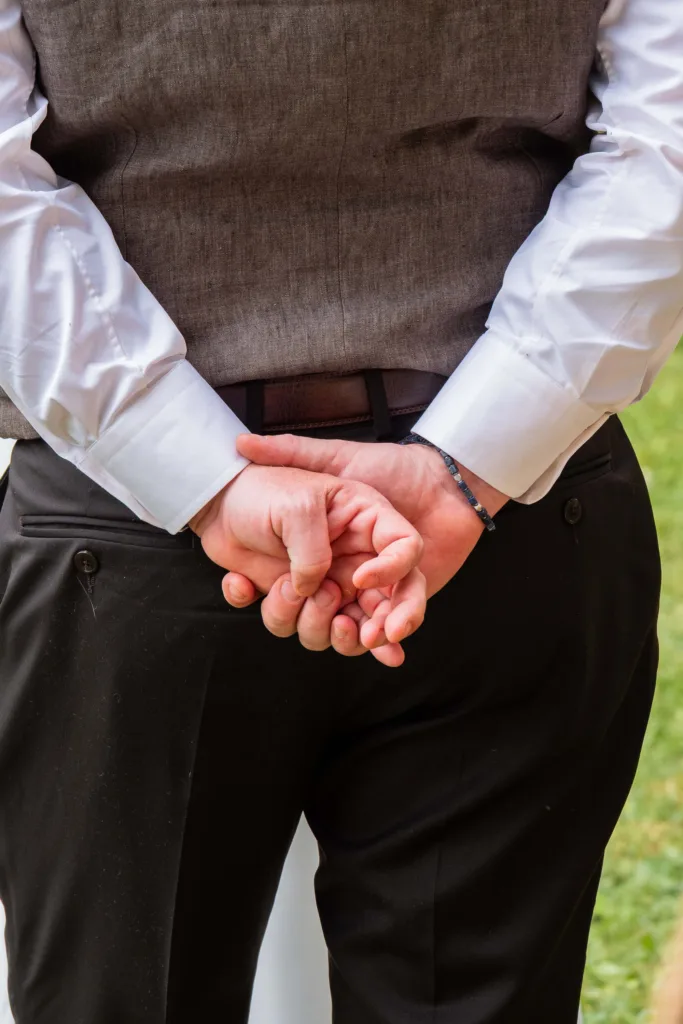 Photo gros plan des mains dans le dos du marié lors de l'échange des voeux à la cérémonie laïque au château du Croisillat à Caraman (31) - Mariage d’Élodie et Julien - 2025 - Photographe à Saint-Gaudens (31) Marc Villard / VILMAGE