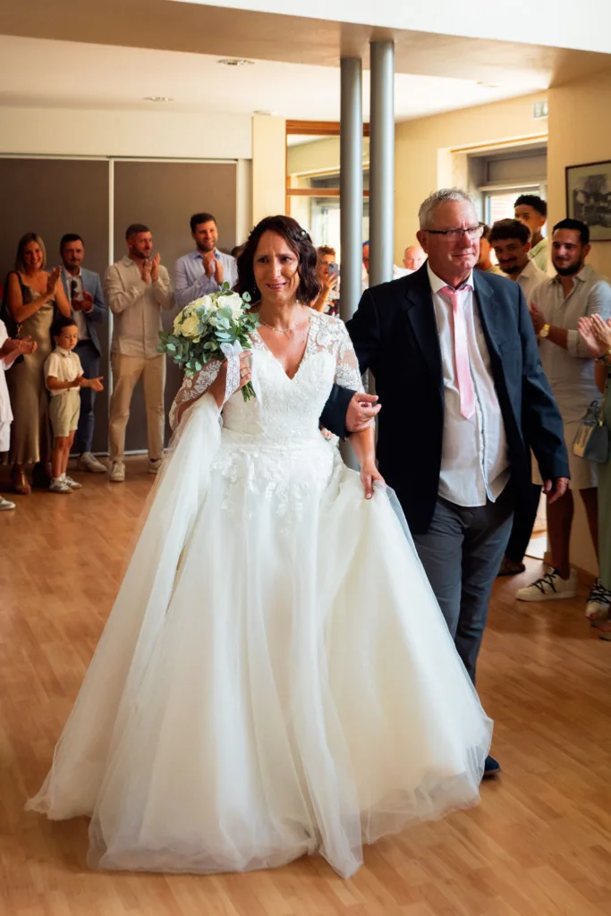 Photo de l'arrivée de la mariée en larme au bras de son père à la mairie de Villeneuve de Rivière (31) - Mariage de Sophie et Alain - 2025 - Photographe à Saint-Gaudens (31) Marc Villard / VILMAGE