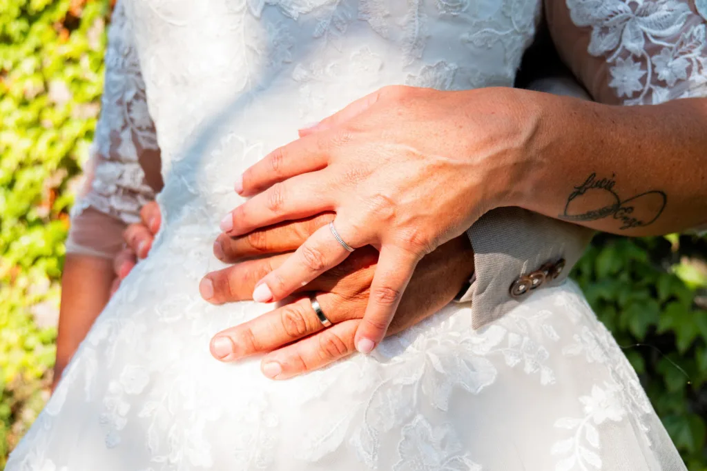 Photo gros plans des mains et des alliances des mariés sur la robe de la mariée - Mariage de Sophie et Alain - 2025 - Photographe à Saint-Gaudens (31) Marc Villard / VILMAGE